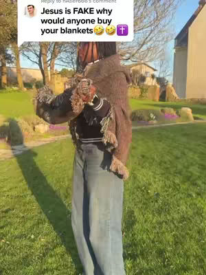 A person wearing a large brown blanket or shawl is standing in the middle of a green field on a sunny day. The person is wearing a black top and jeans, with arms by their sides wrapped by the blanket. A speech bubble is in the top left corner with a comment on the image.
