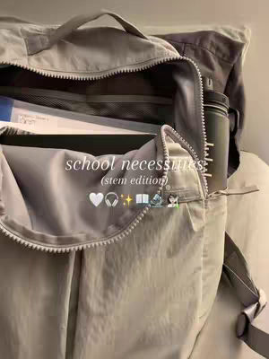 An open backpack stuffed with supplies, with an additional bag in the background. The main backpack is a light grey color. Text overlayed on the image reads 'school necessities (stem edition)' along with some icons.