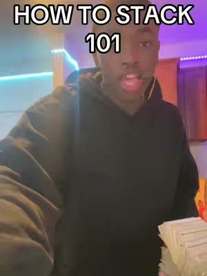 A close-up shot of a young Black man holding a stack of money, with the text 'HOW TO STACK 101' in white letters at the top. The background is blurred, with hints of purple and blue lighting. The man is looking at the camera with his mouth slightly open.