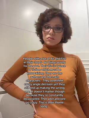 A woman with short, curly brown hair and glasses is centered in the frame, wearing an orange turtleneck sweater. Text in a white box is overlaid with information about astrology.