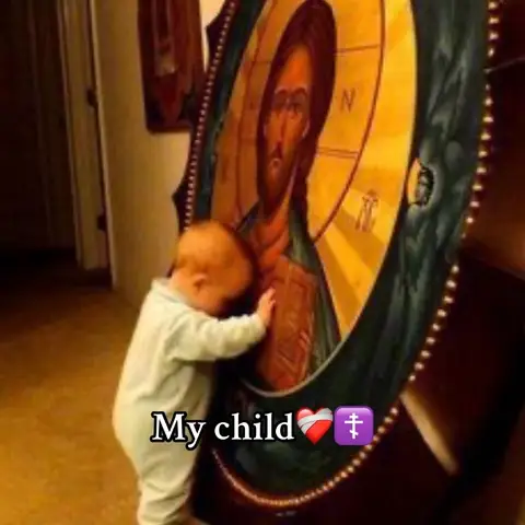 A baby, dressed in light blue, leans against a large icon. The icon depicts a religious figure with a halo and is set in a room with warm lighting. Text overlay at the bottom. The baby seems to be embracing the icon.