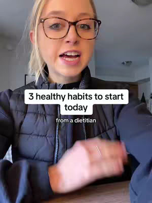 A woman with blonde hair and glasses is centered in the frame, speaking towards the camera at eye level. The background is a blurred indoor setting with neutral tones. A text overlay reading '3 healthy habits to start today from a dietician' is displayed.