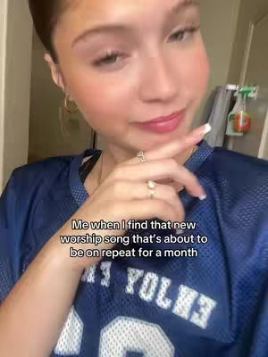 A well-lit selfie featuring a young woman with fair skin, dark hair, and a slight smile. She is wearing a blue football jersey and two rings on her finger. Text is overlaid on the image.