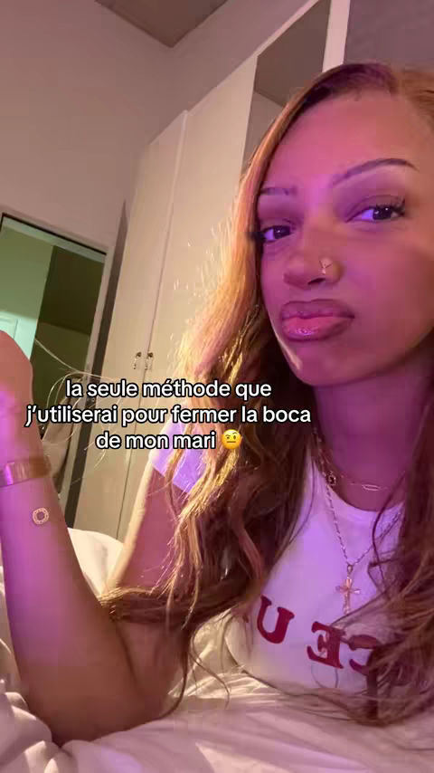 A selfie-style shot featuring a young woman in a bedroom setting. She has long hair and wears a white t-shirt. Text overlays the image with phrases in French.