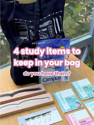 A promotional image showcasing stationery items. The image has a dark navy blue shopping bag, which is open and holds various stationery supplies like pens, notebooks, and other school supplies. Overlaid on top of the bag, in a white and pink font, reads "4 study items to keep in your bag" and below it reads "do you have them?". In the background are wooden tables and plants. The overall composition is aimed to promote and capture the attention of students.