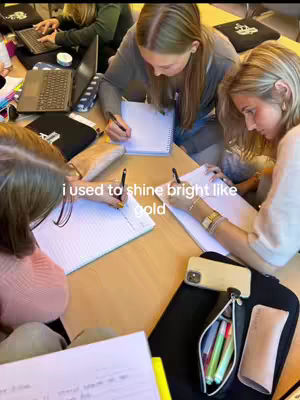 A top-down shot shows a group of young women studying together at a wooden table. The women are all writing on paper. The text overlay says, "i used to shine bright like gold."