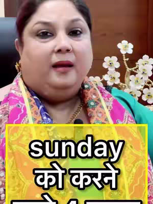 A woman with dark hair and fair skin is centered in the frame, slightly angled towards the camera. She is wearing a colorful scarf, a teal top, and a gold necklace, and a small microphone is clipped to her collar. Behind her, a floral arrangement is visible. A text overlay in Hindi occupies the bottom third of the frame, over an abstract yellow floral background.