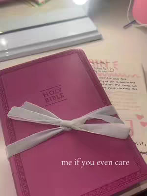 A close-up shot of a pink bible with a decorative white ribbon tied around it. The text "HOLY BIBLE" is printed on the cover. There is some pen-scribbled text, presumably notes, visible in the background. The hook text "me if you even care" is placed at the bottom of the book .