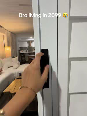 The cover image shows a hand reaching towards a black panel attached to a white wall. The scene has a blurred background featuring a living room setup with a bed and a small wooden table. The overall composition focuses on the action of interacting with the panel, suggesting a futuristic or technological theme.