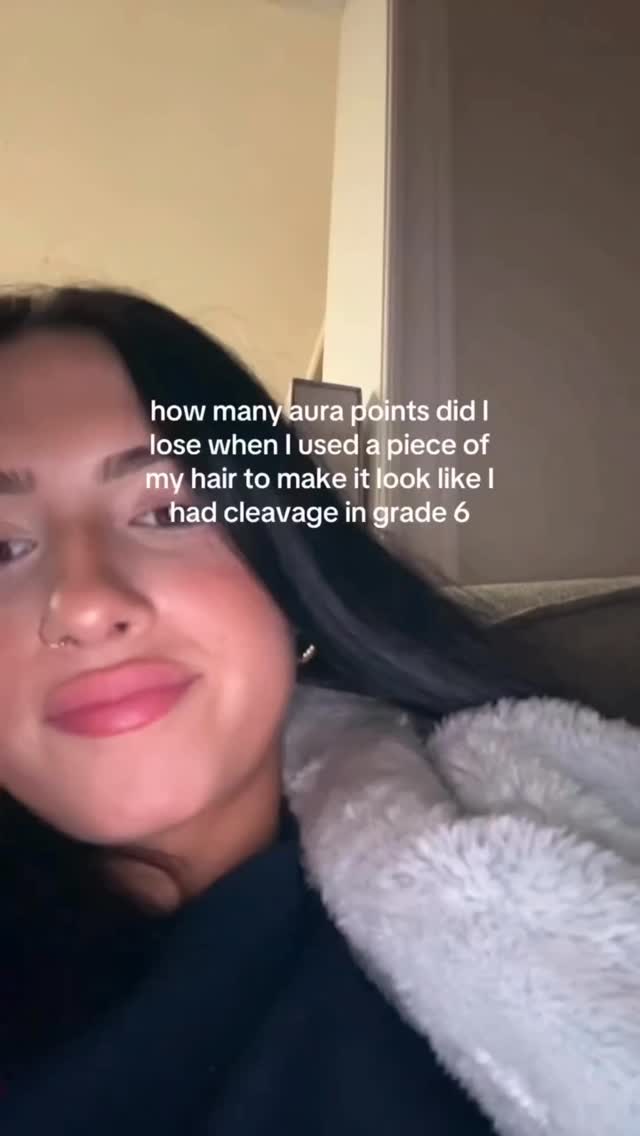 A close-up selfie features a young woman with dark hair and neutral makeup against a blurred background. The text overlay asks a humorous question about her perceived 'aura points' in relation to a past hairstyle.