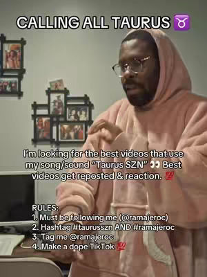 A man wearing a pink hoodie with a sign that says "CALLING ALL TAURUS". The man is looking at something to the right of the screen. In the background are pictures hanging on the wall.