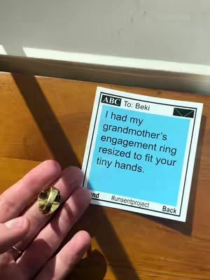 A close-up shot features a hand holding a golden ring, with a sticky note in the background. The note, against a light blue background, has text about resizing a ring. The composition is set on a wooden surface, with shadows adding depth.