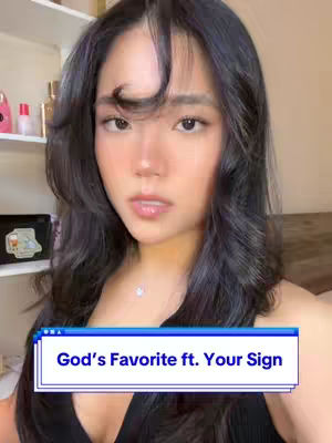 A selfie-style shot features a young woman with long, dark hair and a direct gaze. The background is a soft beige wall with a partial view of a shelf holding small items. A text overlay in a blue box reads, "God's Favorite ft. Your Sign".