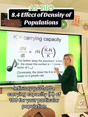 A woman stands in front of a large screen displaying scientific formulas and text related to "Effect of Density of Populations" in a classroom setting. She gestures with a pen, and text overlays appear at the top and bottom of the screen. The overall composition is educational.