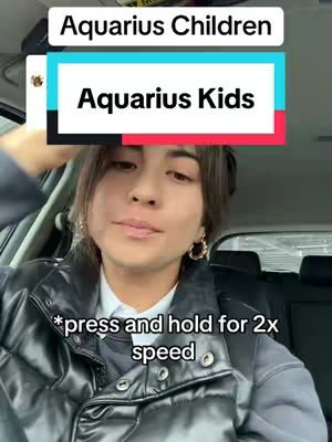A woman is inside a car. She is the main subject, facing forward with a slightly raised expression. Text overlays identify the video with astrology and prompts on how to play the video. The background includes the car interior.