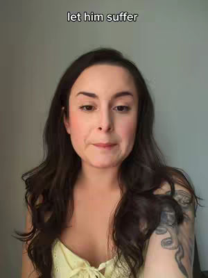 A selfie-style shot featuring a woman with long, dark hair and a soft, neutral background. She is positioned with her upper body visible and is wearing a light-colored top, The text overlay at the top says: "let him suffer."