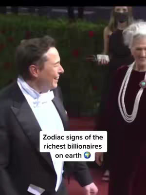 The image shows a man in a tuxedo smiling and looking to his left, appearing to be at an event. He is on a red carpet with another person to his right. Overlayed on the bottom is a white rectangle of text that says, "Zodiac signs of the richest billionaires on earth" with a globe icon. In the background, there is a woman wearing a black dress and a mask.