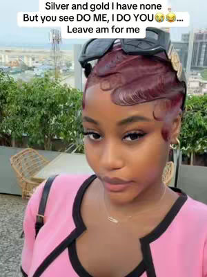 A woman with dark skin and red hair is the focus. She wears a pink top, and has sunglasses perched on her head. The background shows a cityscape and greenery. Text overlaid on the image.