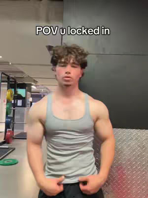 A muscular man in a grey tank top stands in a gym, looking directly at the camera, with text overlayed above.