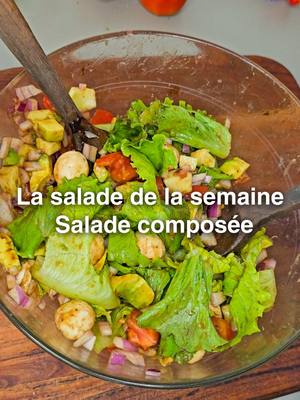A top-down shot on a wooden surface features a clear glass bowl filled with a colorful salad. The salad includes green lettuce leaves, red and yellow tomatoes, white mozzarella balls, purple onion pieces, and other vegetables. A wooden serving spoon rests in the bowl. The image has a soft focus with natural lighting, enhancing the fresh and healthy appearance of the salad. Text overlays in white are visible on the salad, providing context about it.