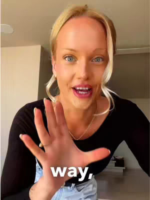 A woman with blonde hair and blue eyes is reaching out towards the camera with her right hand, palm facing forward, with part of her open palm facing the camera. Text is overlaid on her palm area. She is wearing a black top, and light shines from a light source. Behind her is a neutral-colored room and furnishings.