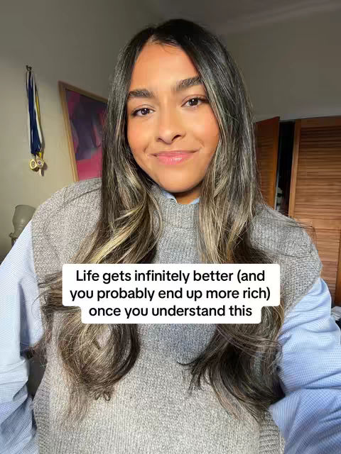 A young woman with long hair and a grey sweater is the main focus, smiling gently at the camera. A text box provides the hook in white, with the text: Life gets infinitely better (and you probably end up more rich) once you understand this. The background includes a wall with a painting, a door and parts of a room.
