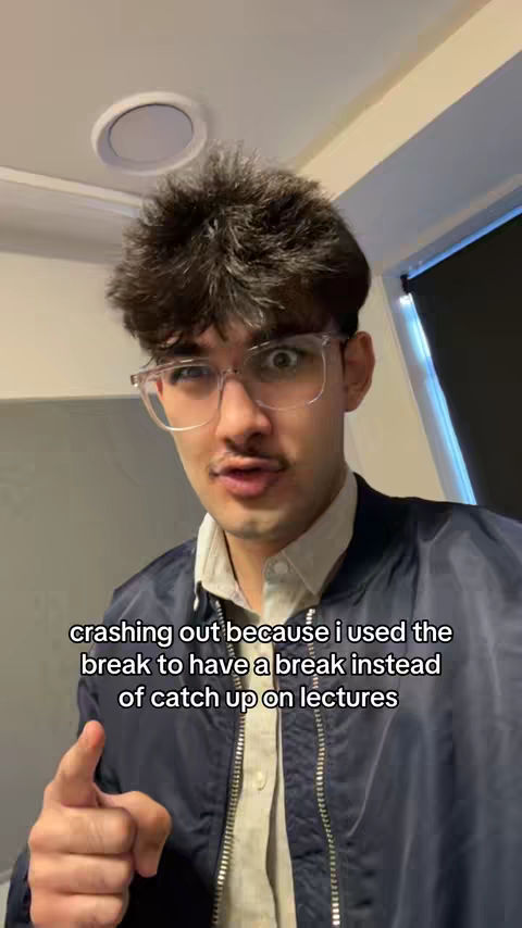 A young man with dark hair, mustache, and glasses stares wide-eyed at the camera, pointing. He wears a white shirt under a black bomber jacket. Text overlays the image.