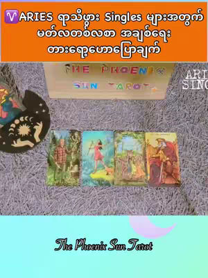 The image features four tarot cards laid out on a purple surface, with a wooden box that says "THE PHOENIX SUN TAROT." Above the cards is an orange banner containing text in a foreign language, with gold text placed over it. Below the cards is the name "The Phoenix Sun Tarot" in a cursive font over a light blue gradient. A white design of a circle with a crescent moon is on the left side.