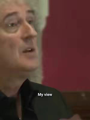 A medium shot shows a man, presumably Brian May, speaking. The background is dark red. Text overlayed on the image says, "My view."