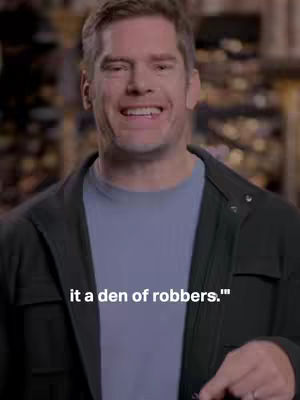A man in a black jacket and blue shirt looks towards the camera and smiles. Text overlayed on the image.