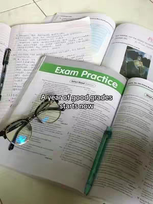A top-down shot shows open books with handwritten notes, an open exam practice book, and a pair of glasses. Text overlayed on the book reads A year of good grades starts now.