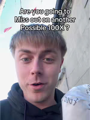 A young man with light skin and short, light-brown hair is centered in the frame. He has a slight smile and appears to be speaking. Above his head is overlay text in a bold, sans-serif font. The background is a blurry mix of outdoor elements, suggesting a daylight setting. In the right hand of the man is white object.