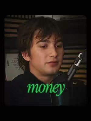 A young man with dark hair and a black shirt is centered in the frame. The background is softly blurred, with hints of bookshelves and possibly a microphone stand visible. The word "money" is overlaid in a vibrant green font near the bottom of the frame.