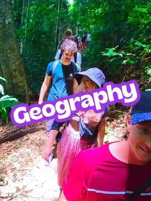 A group of people are hiking on a trail through a forest. The image has a natural, outdoorsy feel with lush green foliage surrounding the path. A large, purple text overlay states 'Geography'. The hikers are dressed in casual clothing, and the overall impression is one of adventure and exploration.