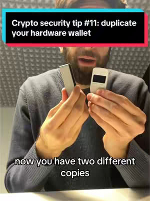 A man with a beard holds two hardware wallets, one in each hand, against a grey background. Text overlays highlight the crypto security tip. The man looks surprised or concerned.