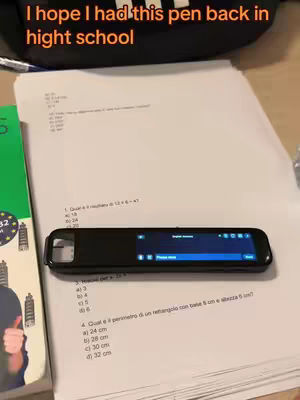 An image showcasing a black, rectangular smart pen resting on top of a stack of papers filled with handwritten math problems. The pen's screen displays a user interface with a 'English scanner' prompt. Above, overlaid text says, 'I hope I had this pen back in hight school.'