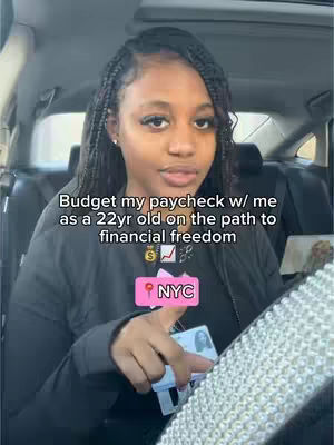 A woman with dark hair and braids is seated in a car, looking towards the camera. Text overlays state "Budget my paycheck w/ me" and "NYC". She is holding a card and pointing to something. The background is the interior of a car.
