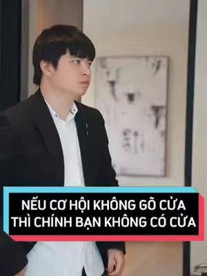 A man in a black blazer and white shirt looks off to the side, with a blurred background of a painting. At the bottom is a text overlay.