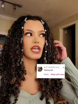 A young woman with curly hair, adorned with silver hair accessories, gazes slightly upward with an open mouth in a gesture of surprise or expression, a comment section with the word 'Taurus' is on screen.