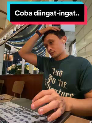 A man in a dark green shirt rests his hand on his head, looking at a laptop in front of him. The background is slightly out of focus, suggesting an indoor location, likely a cafe or workspace. Above him is a teal bar with white text.