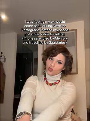 The cover image is a selfie-style shot featuring a woman in a room. She is framed from the chest up with the main background in focus. The upper body of the figure is visible. On the lower part of the image, the person wears a cream colored sweater and a red and yellow beaded necklace. The woman has dark, short, curly hair and dark makeup. She is making a kissing face. In the upper right part of the image there is a framed picture on the wall. On the left is the corner of something brown, which could be a coat rack. The text overlays the image in the middle top. The room is dimly lit, which creates a focus on her.