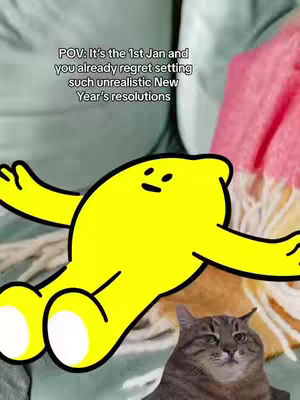 The image shows a cheerful yellow lemon-shaped cartoon character with arms outstretched, set against a background of fabric in shades of green, pink, and yellow. Below the lemon, a cat looks forward at the camera with a mildly concerned expression.