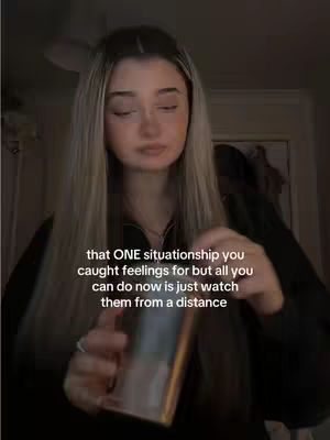 The cover image shows a young woman with long blonde hair, slightly blurred, holding a golden phone. Text overlayed on the image reads: "that ONE situationship you caught feelings for but all you can do now is just watch them from a distance". The background is dark and out of focus.