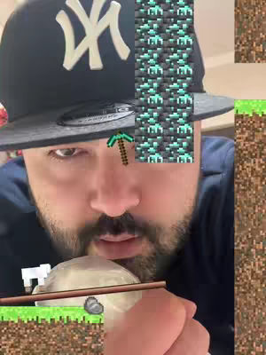 A close-up shot of a man's face, wearing a black baseball cap with a white 'NY' logo. A Minecraft-themed overlay is placed on his forehead and a white object, resembling a cloud, floats near his mouth. The background is pixelated to simulate a Minecraft setting.
