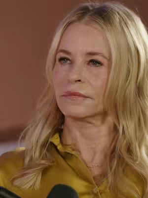 The cover image features a close-up shot of a woman looking towards the left. She has blonde hair and is wearing a mustard-colored top. Her expression is serious, with her lips slightly pursed. The background is a blurry shade of brown.