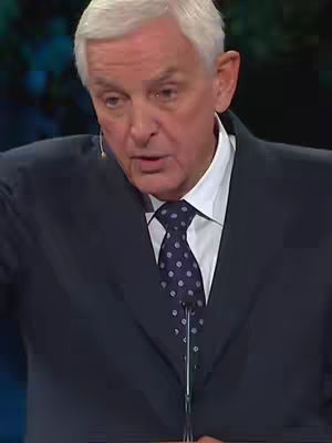 The cover image features a man in a suit speaking, likely in a studio setting. The background is blurred with shades of green and blue, indicating a professional environment. The man is the central focus, positioned from the chest up, wearing a dark suit, white shirt, and a patterned tie. The lighting suggests it's a studio environment, with the man holding a microphone.
