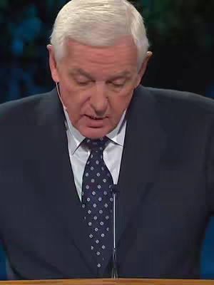 The cover image shows a head and shoulder shot of a man in a dark suit, white shirt, and patterned tie. He has short, white hair and is looking down with a serious expression. There is a microphone near his face.