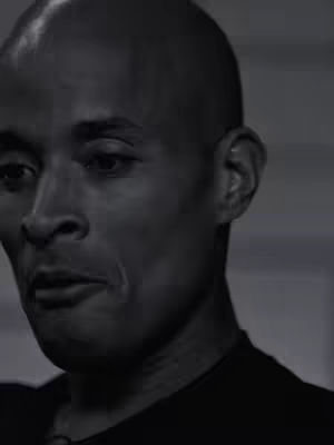 A grayscale close-up of a man looking down, with a focused expression, set against a blurred background.