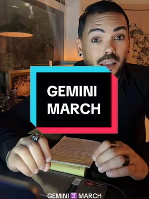 A man with dark hair and a beard is centered in the frame, looking directly at the camera. Behind him is a blurred interior space. Overlaid on the image is a rectangular graphic with the words 'GEMINI MARCH' displayed in white text against a black background, bordered by turquoise and red frames. The man is wearing a black shirt, rings, and earrings.