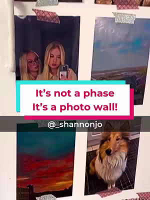 The cover image showcases a photo wall with various framed photos attached to the wall with tape. In the center is a text overlay in a colored box that reads "It's not a phase, It's a photo wall!". To the left is a photo of two females looking at a phone, and at the bottom-right is a dog. The rest of the photos are of different scenes.